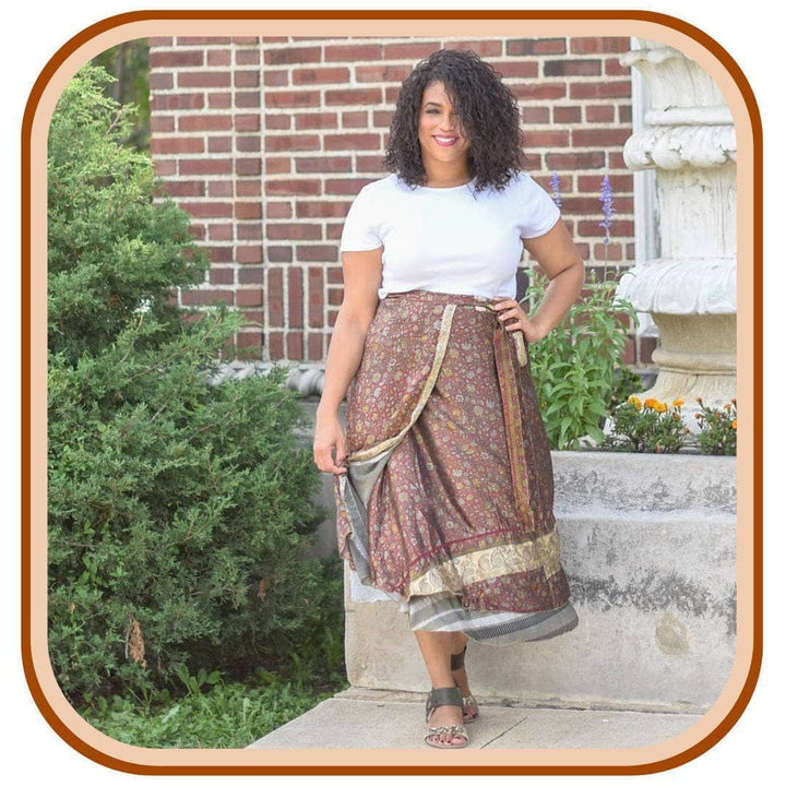 Model standing outside with a tree next to her. She wears a light brown sari wrap skirt that has a black and white stripe pattern underneath. She is wearing a white t shirt along with black sandals.