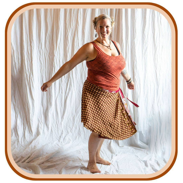 Model stands against a white background. She wears an orange tank top and a light orange pock-a-dot sari wrap skirt. The skirt is brown with orange pock-a-dots all over, it also has a red belt.