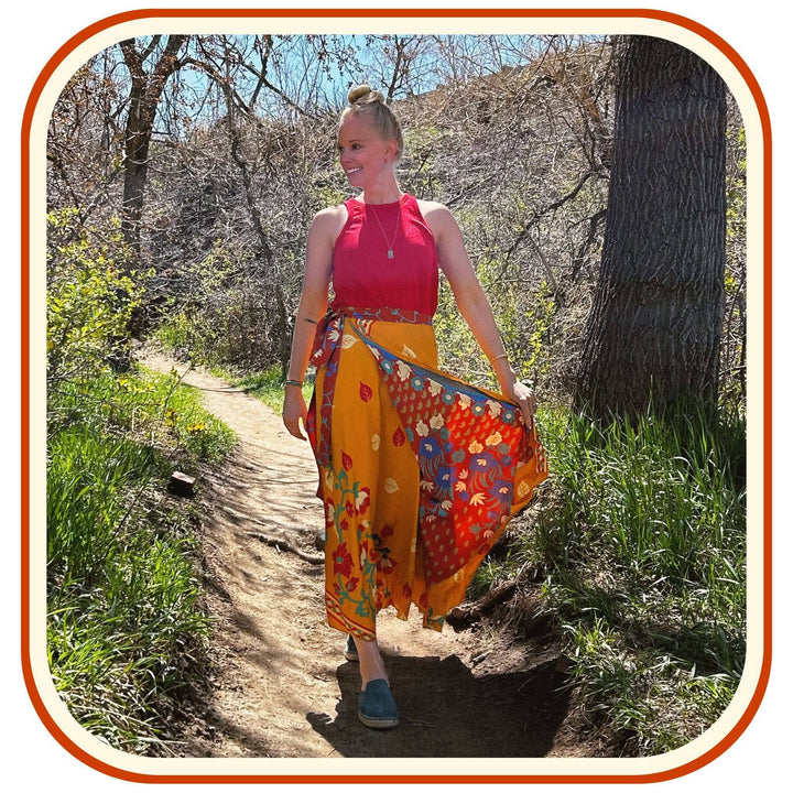 Model is outside on a walk with trees in the background. She wears a bright red top and a sari wrap skirt. The skirt is a light orange with a red floral pattern.