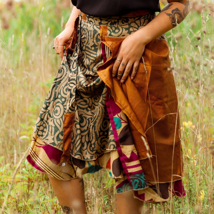 model is wearing an orange and green fall mini sari wrap skirt  while standing in tall grass. 