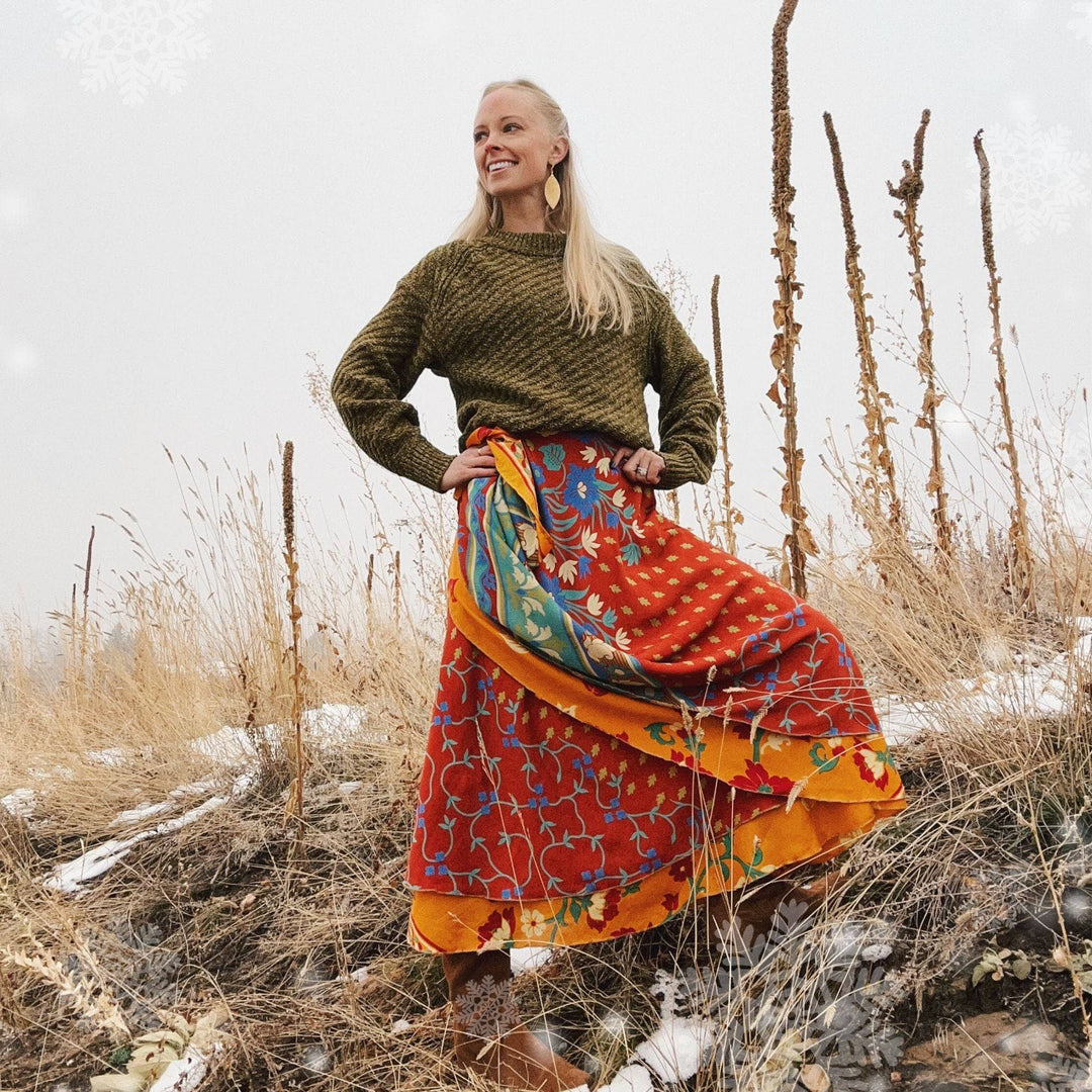 Girl wearing a dark orange sari wrap skirt. She is standing in a forest with very little snow around her.