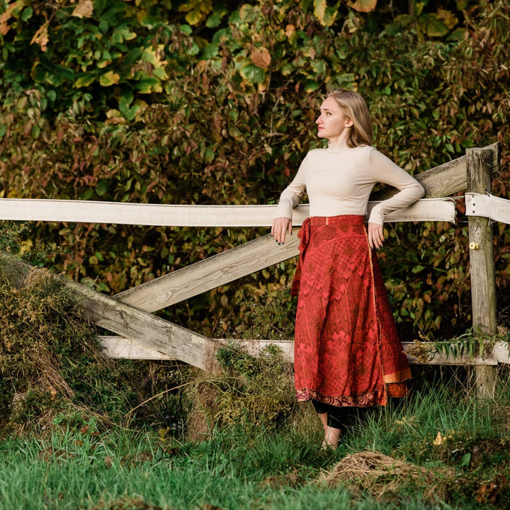 Model is standing next to a fence wearing a red maxi sari wrap skirt 
