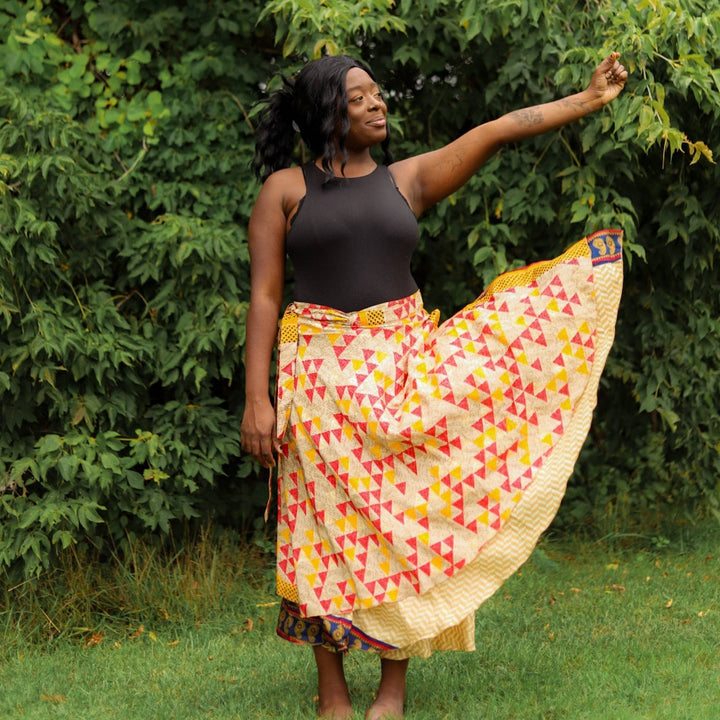 Model is standing grass and just let go of the corner of their yellow sari wrap skirt  to let it flow in the wind. 