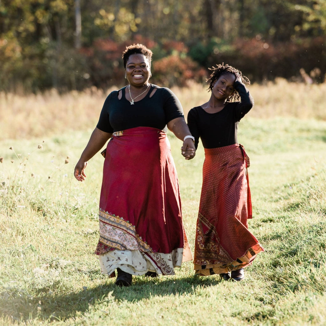 Two models are walking in a field wearing maxi length red sari wrap skirts. 