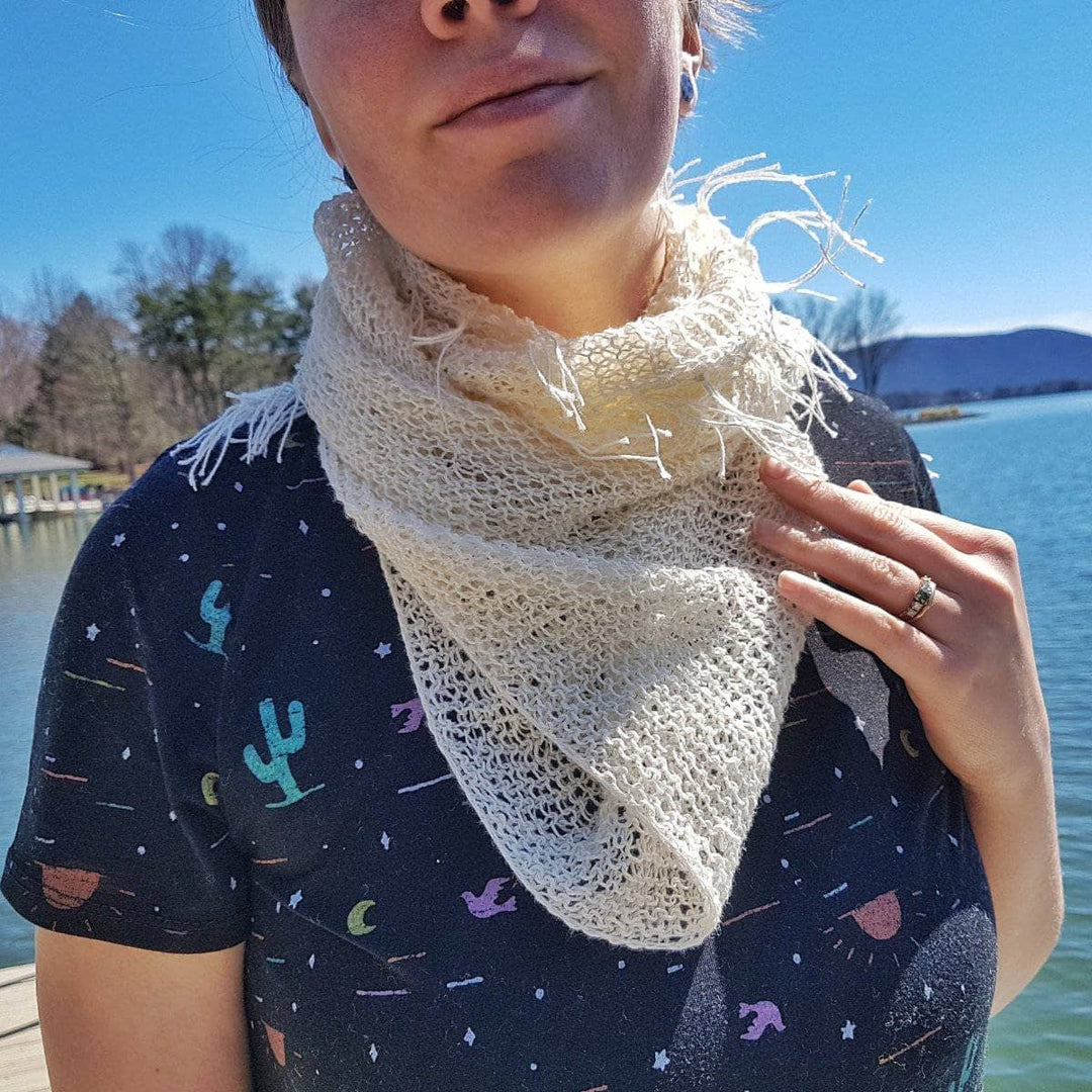 A woman wearing a white cowl around her neck outside by a lake 