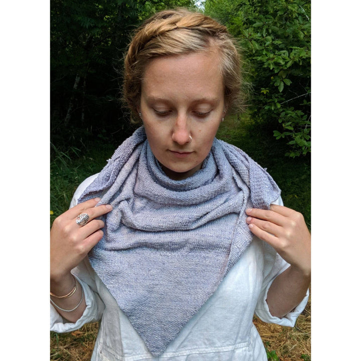 Model wearing serendipity lace weight shawl in grey in front of a wooded background. 