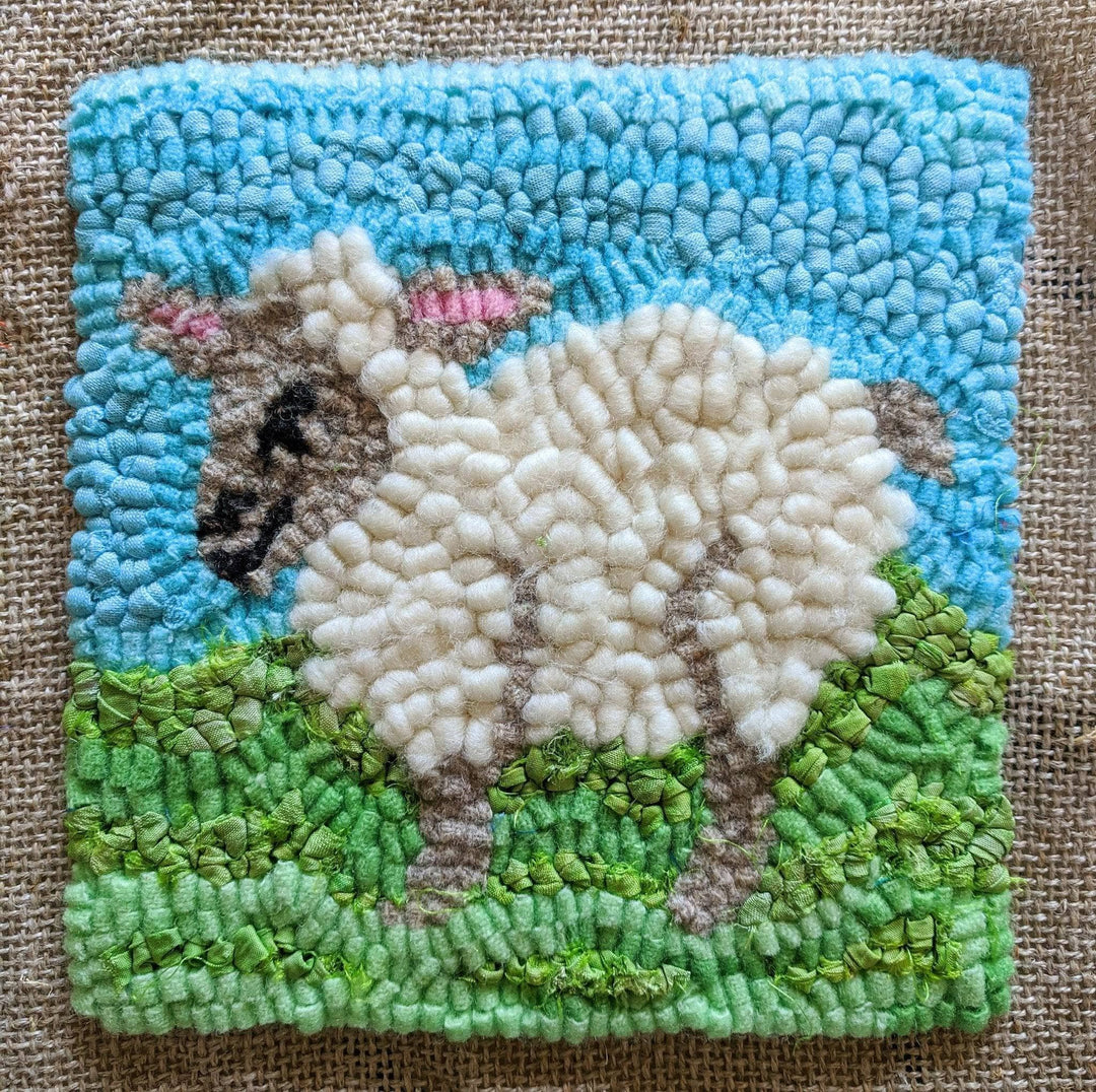 rug hooked sheep in green field with blue sky in front of a canvas background.