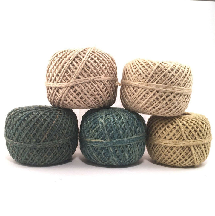 A tan, dark, tan, dark green, light green, and light yellow green cakes of yarn on a white background