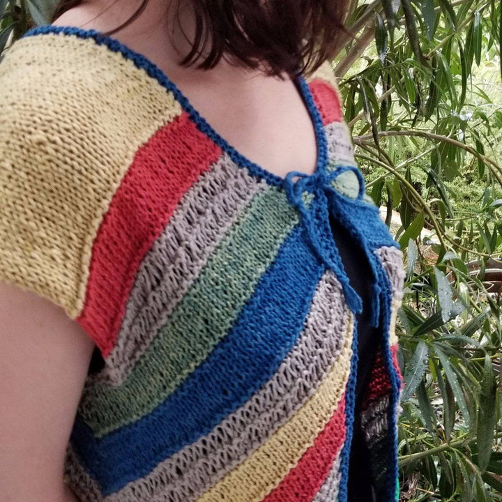 A side view of a women wearing a yellow, red, tan, green and blue stripped cardigan with trees in the background