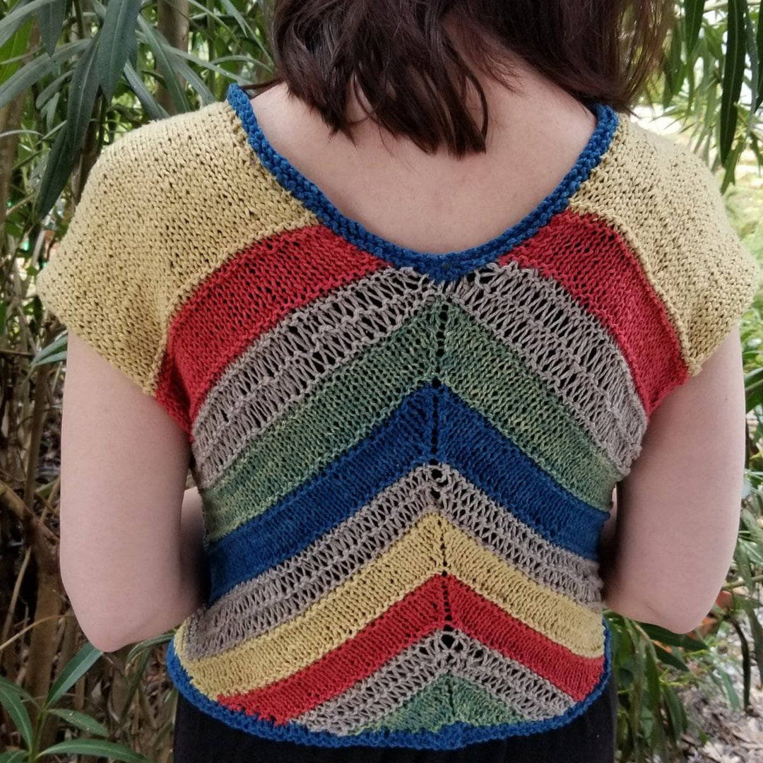 A back view of a women wearing a yellow, red, tan, green and blue stripped cardigan with trees in the background