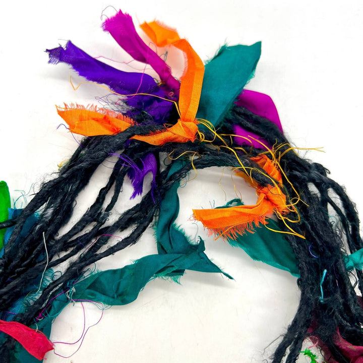 A black skein of banana fiber yarn with multicolored ribbons tied to it on a white background