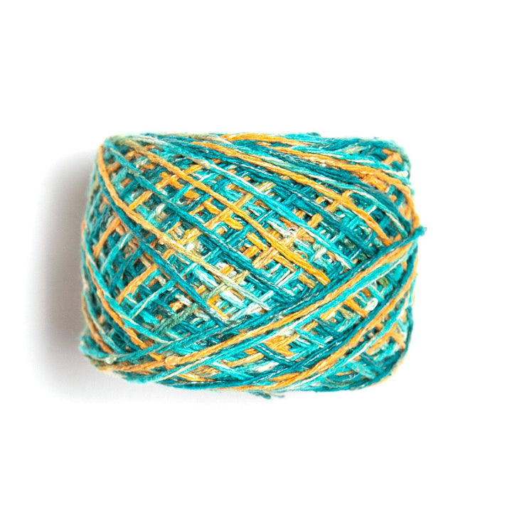 Side view of silk blend sport weight yarn in colorway island glow (turquoise and golden yellow variegated) in front of a white background.