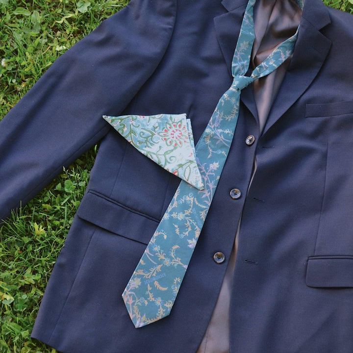 Blue silk neck tie and blue pocket square on a suit jacket in the grass. 