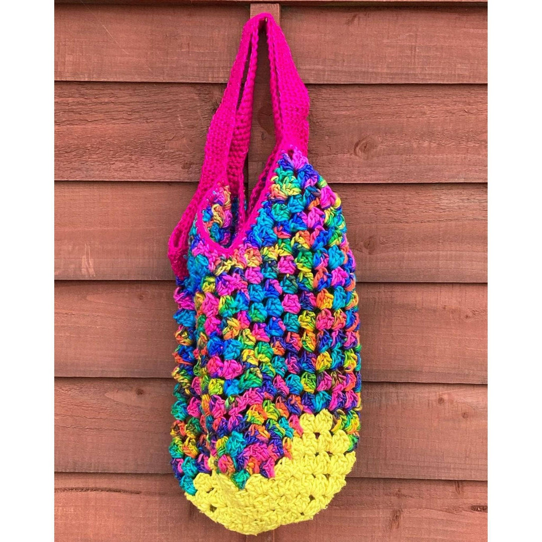 Crochet Bag Made from silk roving worsted weight yarn in illuminating and watercolors hanging in front of a brown wood wall.