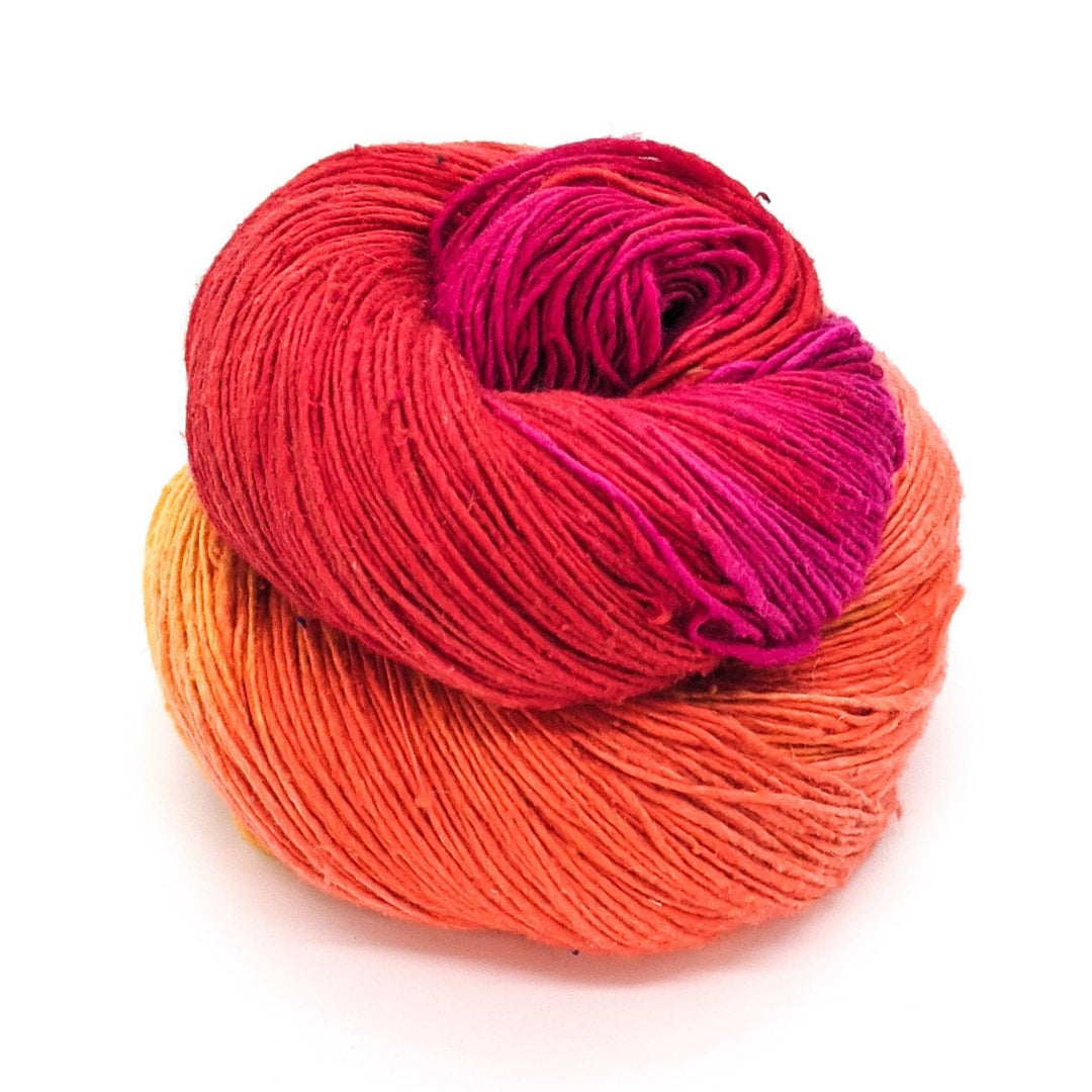 bright pink, red, orange, yellow lace weight silk skein in front of a white background.
