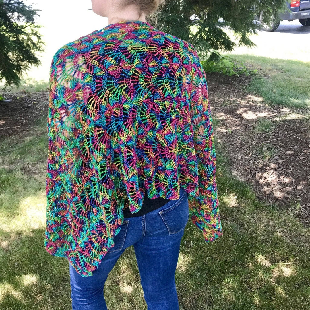 Lace weight silk waves shawl in rainbow colorway being worn by model outside with trees in the background.