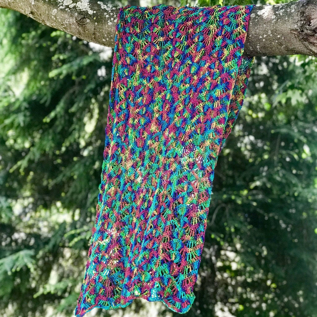 silk waves shawl in rainbow colorway hanging from the branch of a tree.