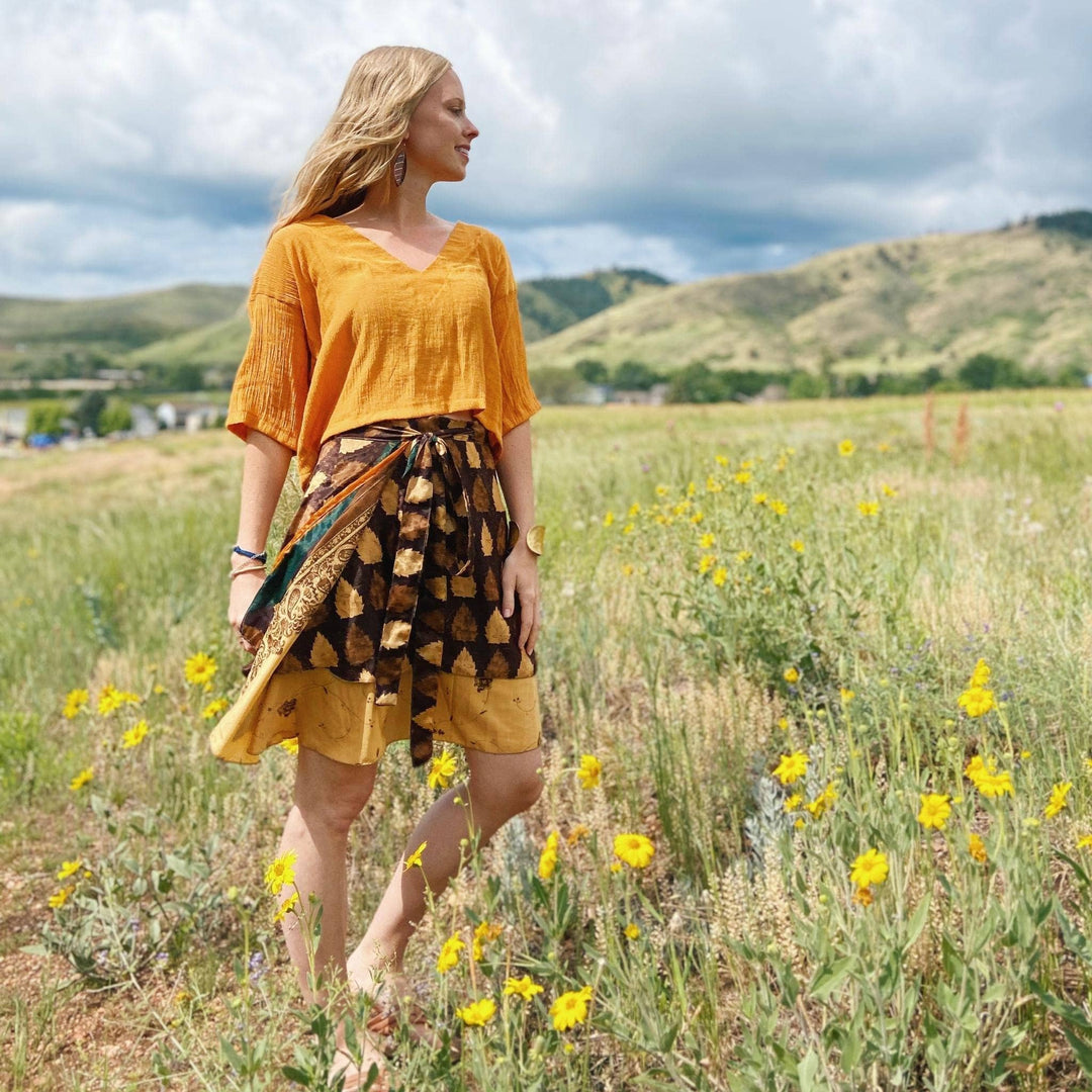 Model is in a field wearing a brown and yellow mini sari wrap skirt. 