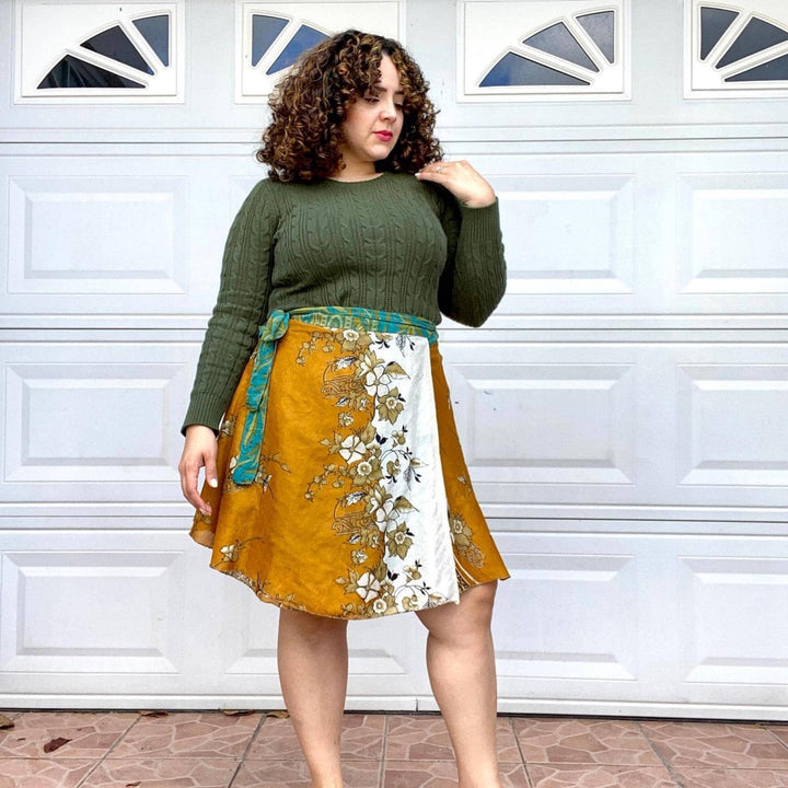 Plus size model is wearing a mustard yellow mini sari wrap skirt while standing in front of a white garage door. 