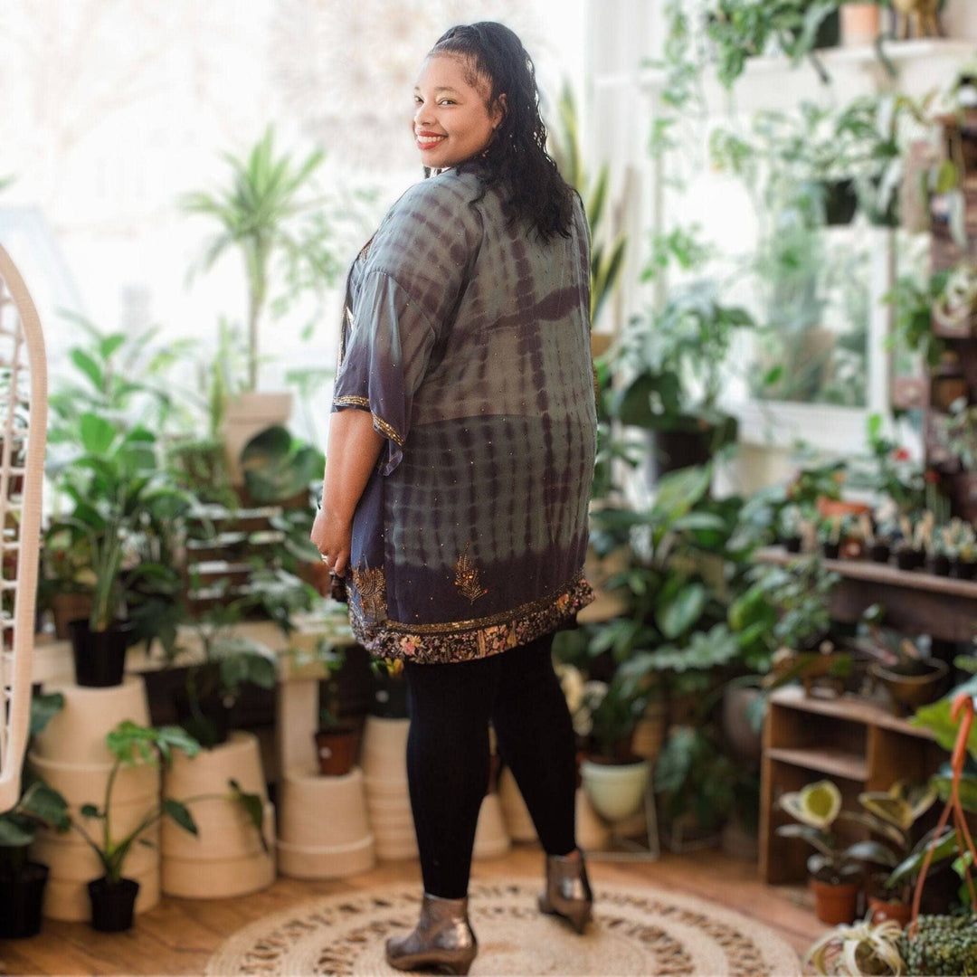 Plus size model is wearing a dark blue tie dye sophia silk duster with potted plants in the background. 