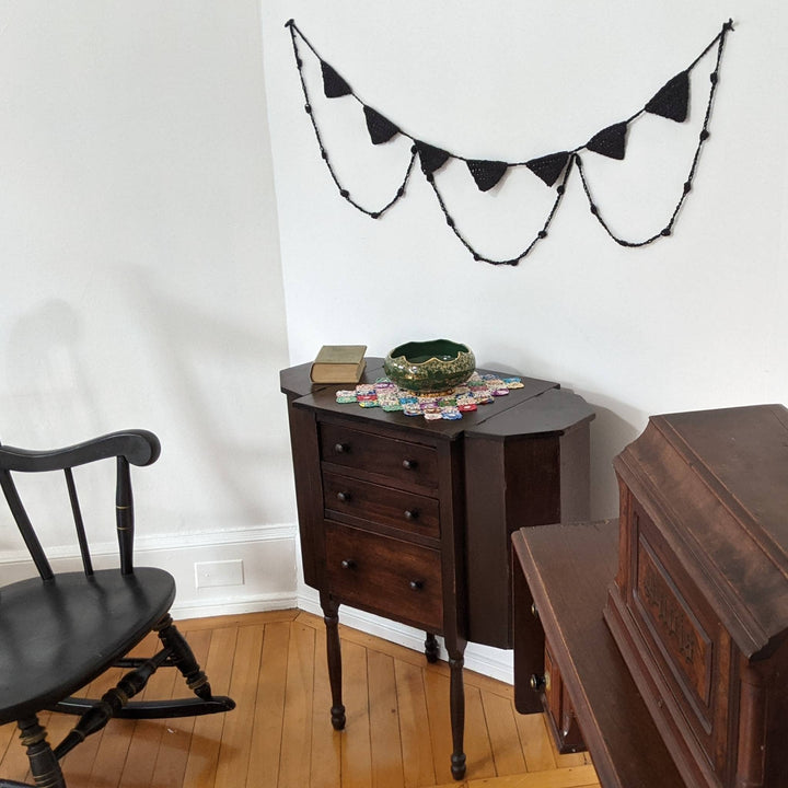 Spooky chic halloween bunting hung on display on a white wall with several pieces of antique dark wood furniture around. 