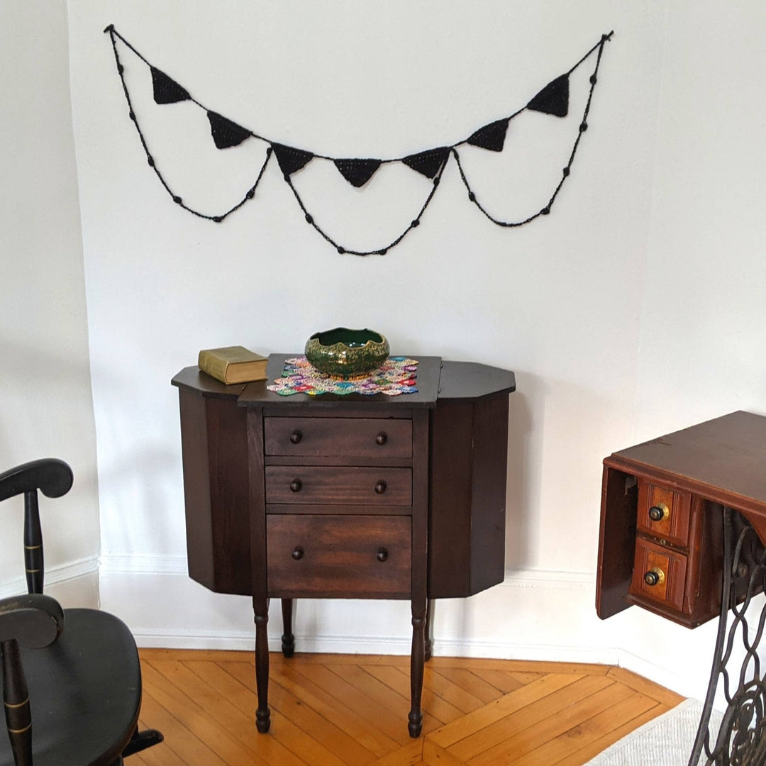 Spooky chic halloween bunting in black hung on a white wall above older pieces of dark wood furniture.