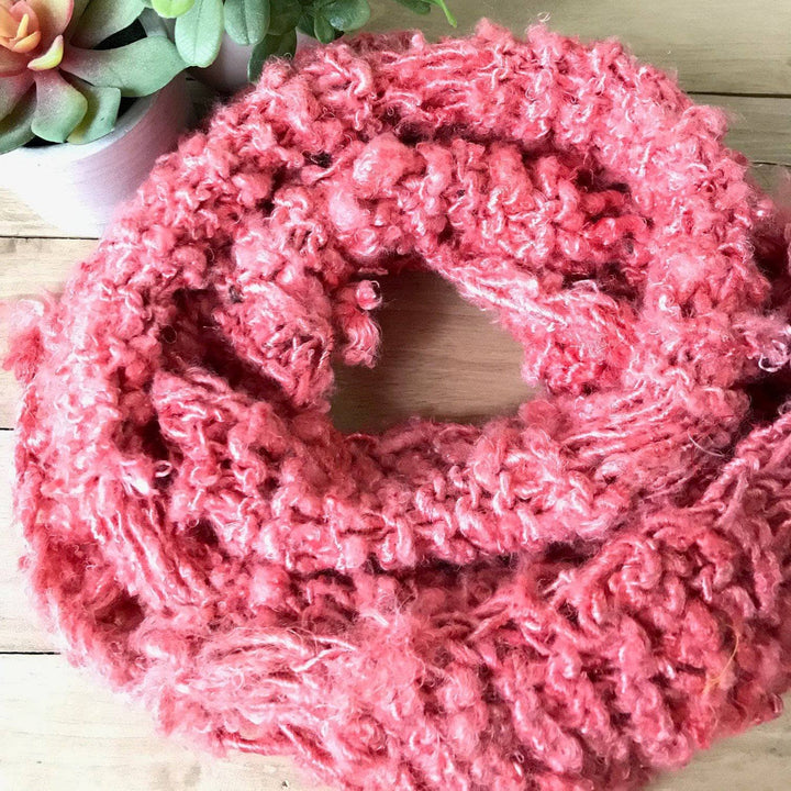 Spring Infinity Scarf in Coral sitting on a wooden background with a small plant