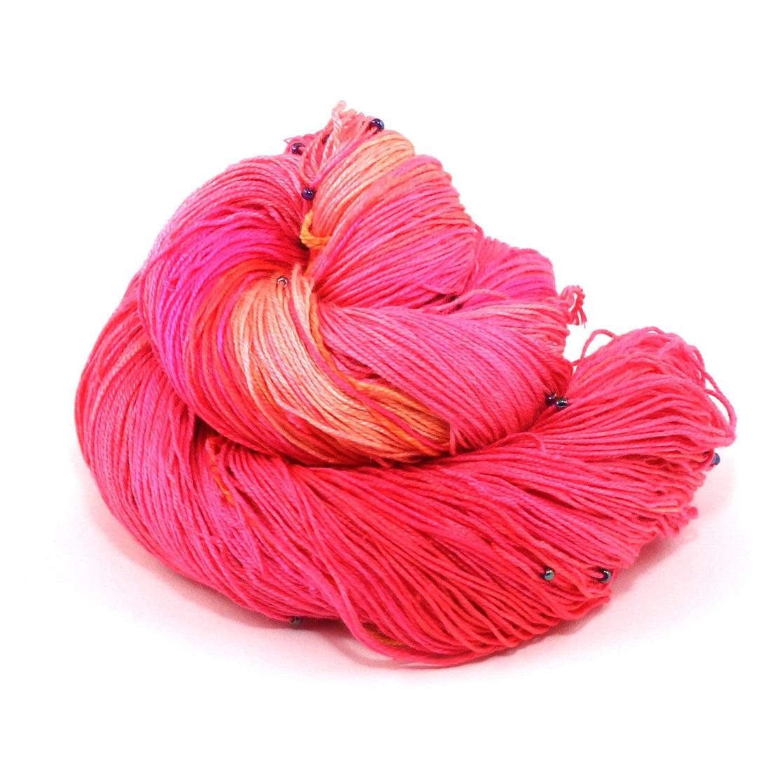 Hand beaded lace weight yarn ball in Tropical Swirl (pink, orange) on a white background