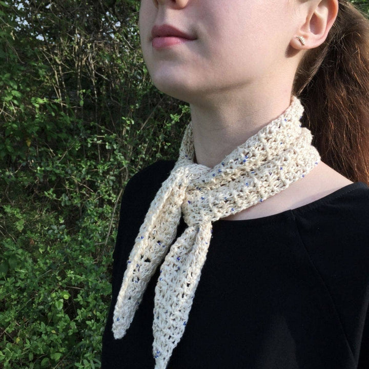 Woman wearing the Springtime City Mini Crochet Scarf in Cream in front of greenery 