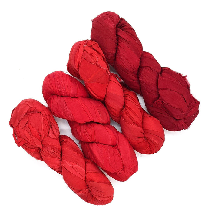 4 skeins of red ombre ribbon yarn on a white background