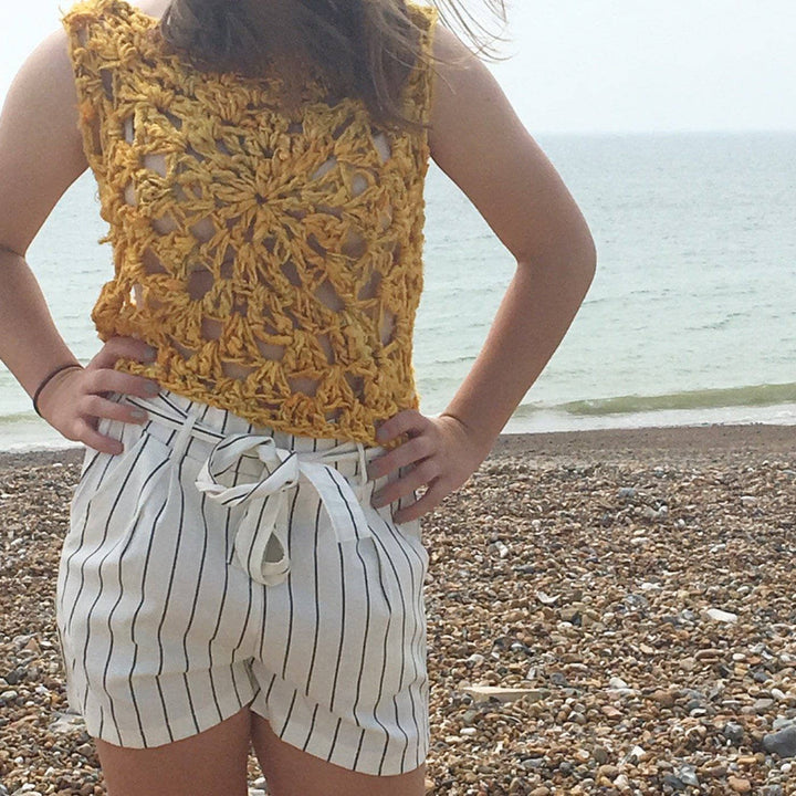 Woman wearing the Sunny Days Tank Top in Sunflower (yellow) in front of a beach