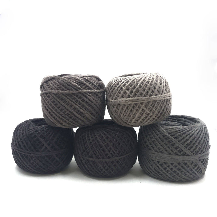 A light gray, medium gray, dark gray, light brown and dark charcoal cake of yarn sitting on a white background