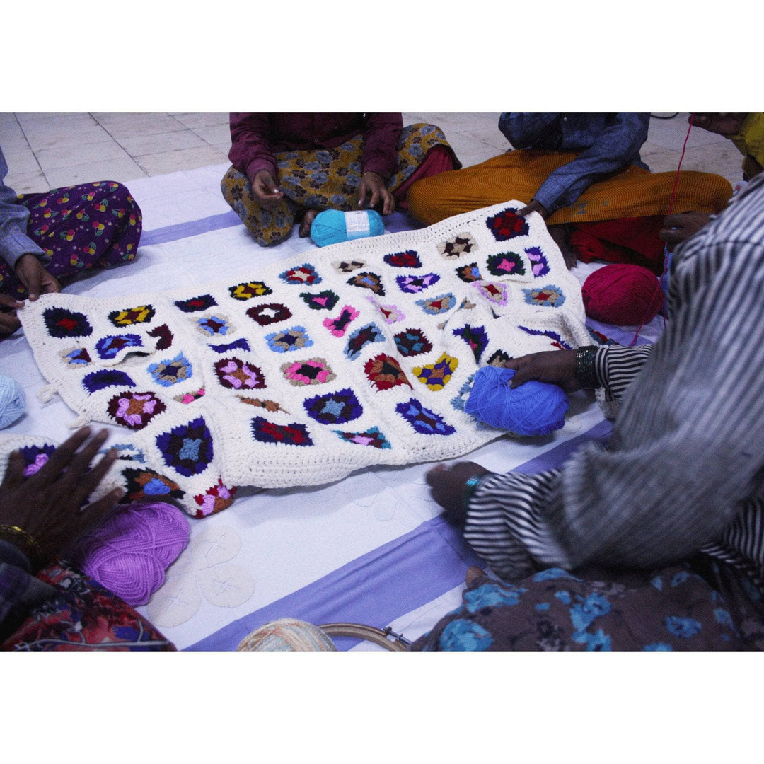 Image of women at a co-op in India joining granny squares for a technicolor long cardigan. 