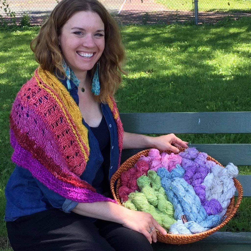 Woman wearing That Sunset was Bananas! Shawl sitting on a park bench with large basket full of banana fiber yarn
