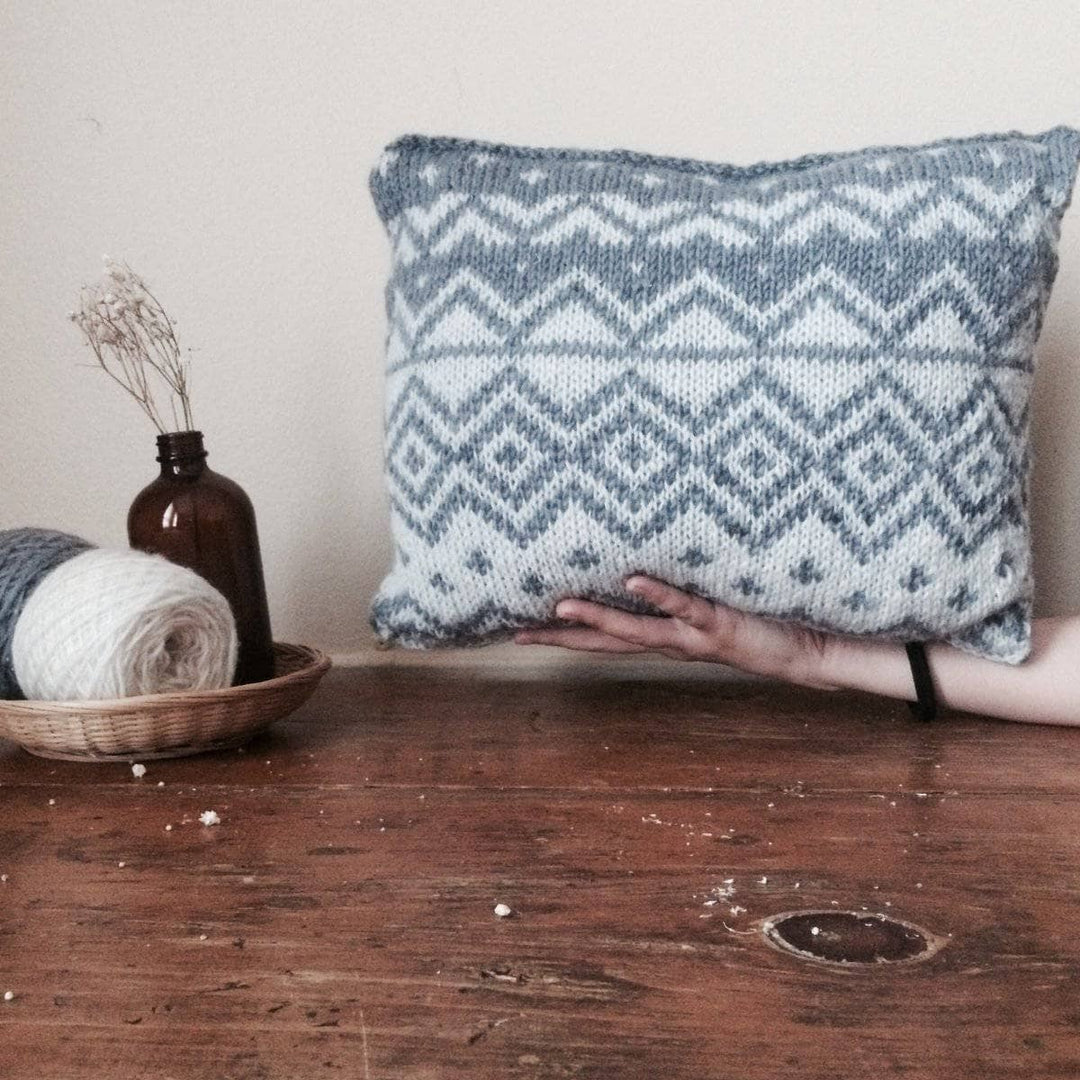 The Bjerge Pillow held by woman's hand over a wooden table