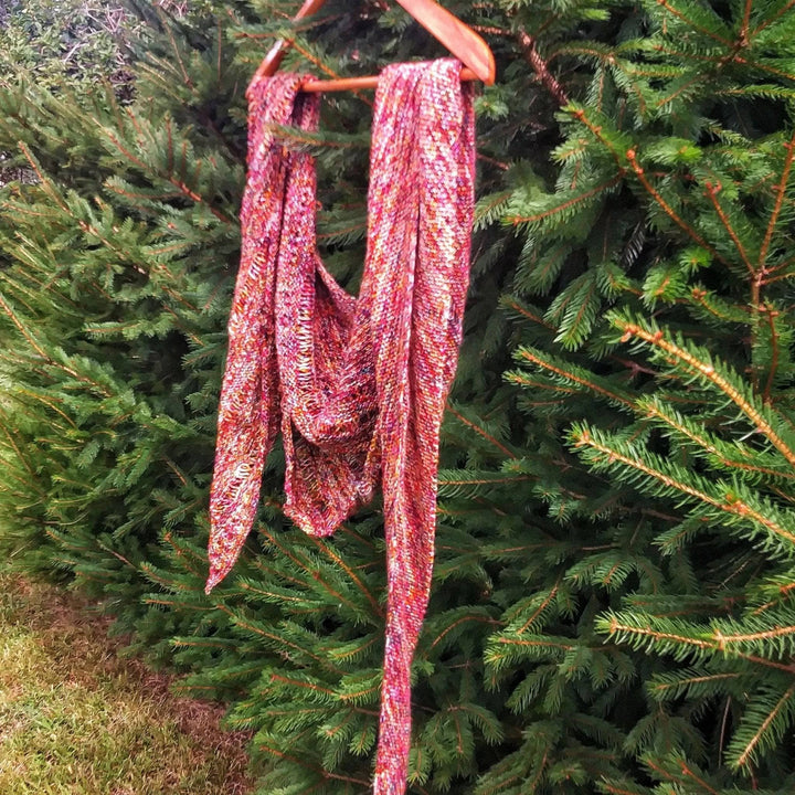 A specked red and yellow shawl hanging on a hanger on a tree