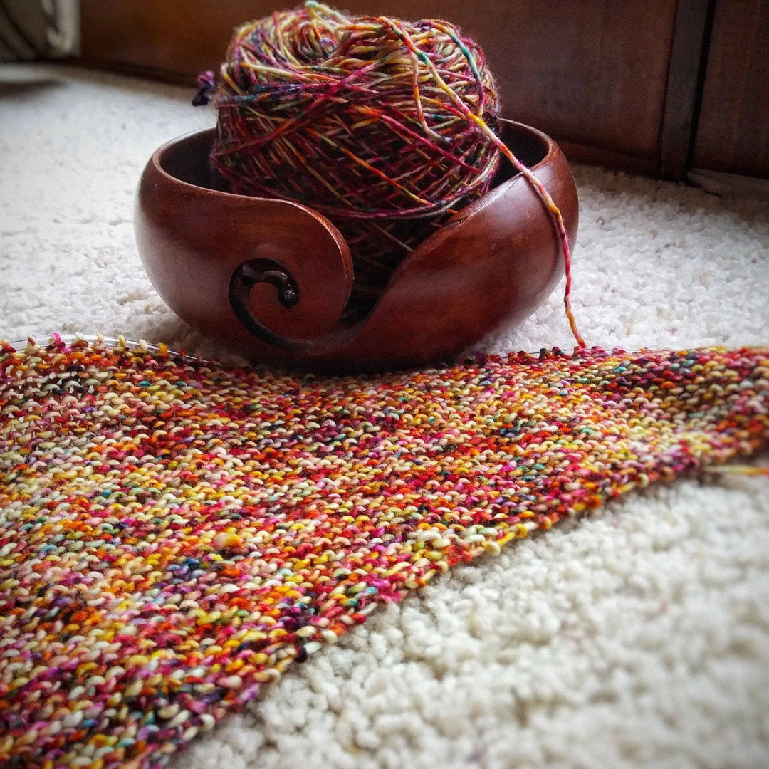 In progress picture of a red and yellow speckled shawl with a yarn bowl in the top of the picture on a white background