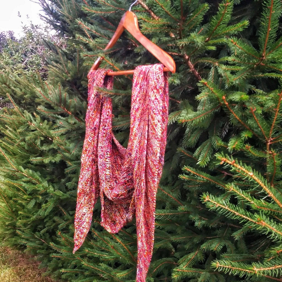 A specked red and yellow shawl hanging on a hanger on a tree