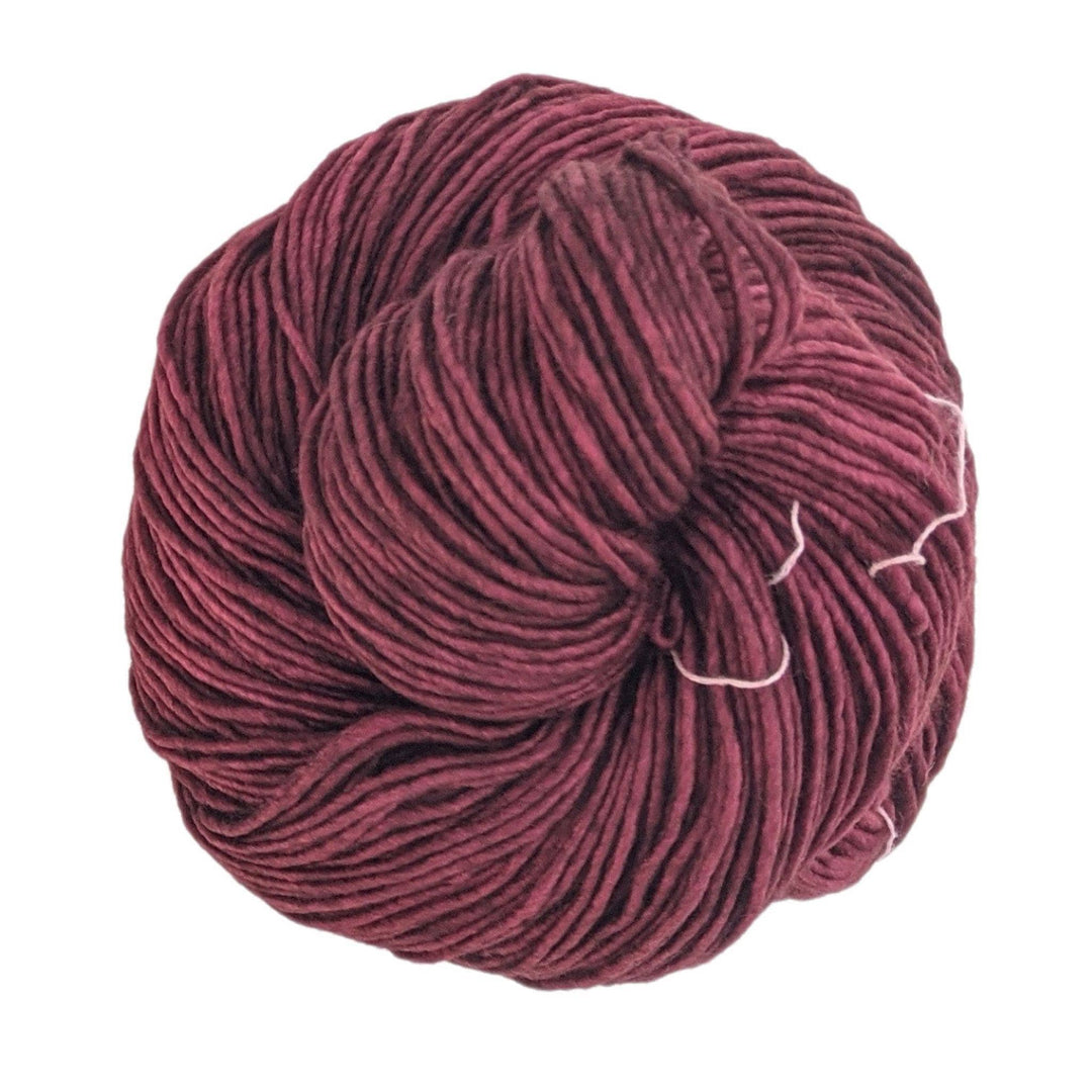 skein of single ply malabrigo wool yarn in tonal red colorway in front of a white background.