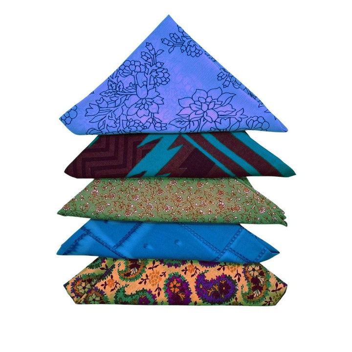 Five assorted furoshiki tied as triangles laying on a light yellow backdrop.