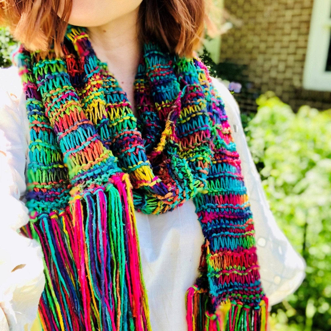 model wearing rainbow knit scarf with greenery in the background.
