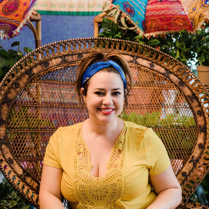 Model wearing blue and gold one of a kind kameela knot headband and pony tail with wicker chair in the background 