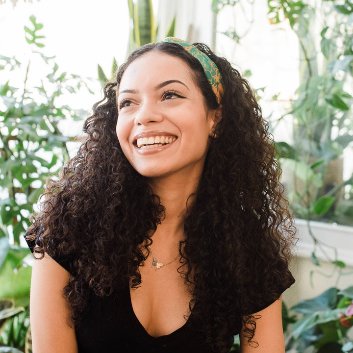 Model wearing green and orange kameela knot headband with greenery in the background.