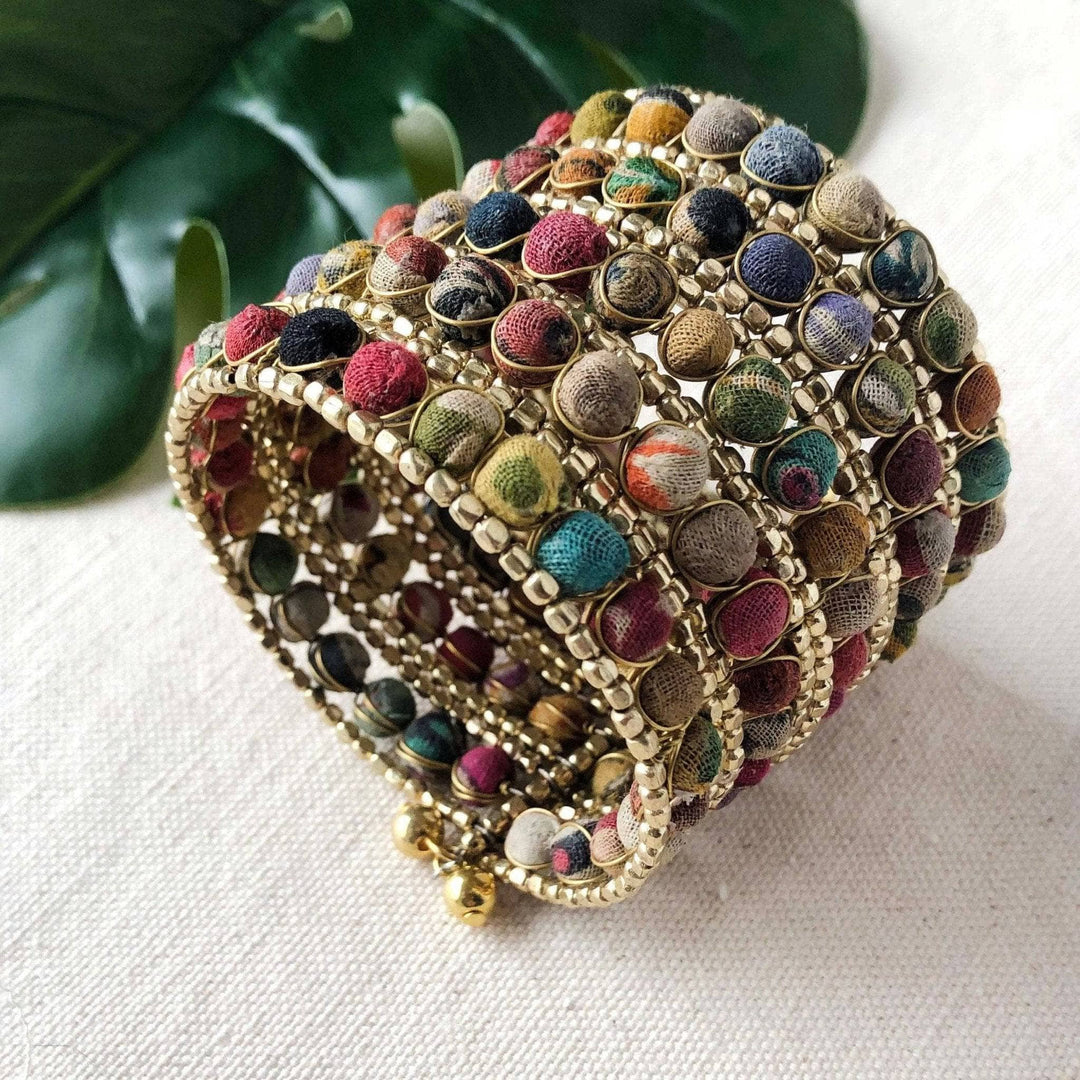 A multicolored Kantha beaded cuff bracelet made with gold beads and wire on a background of cloth.