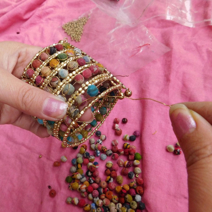 A picture of a woman artisan's hands as she is creating a beaded Kantha cuff.