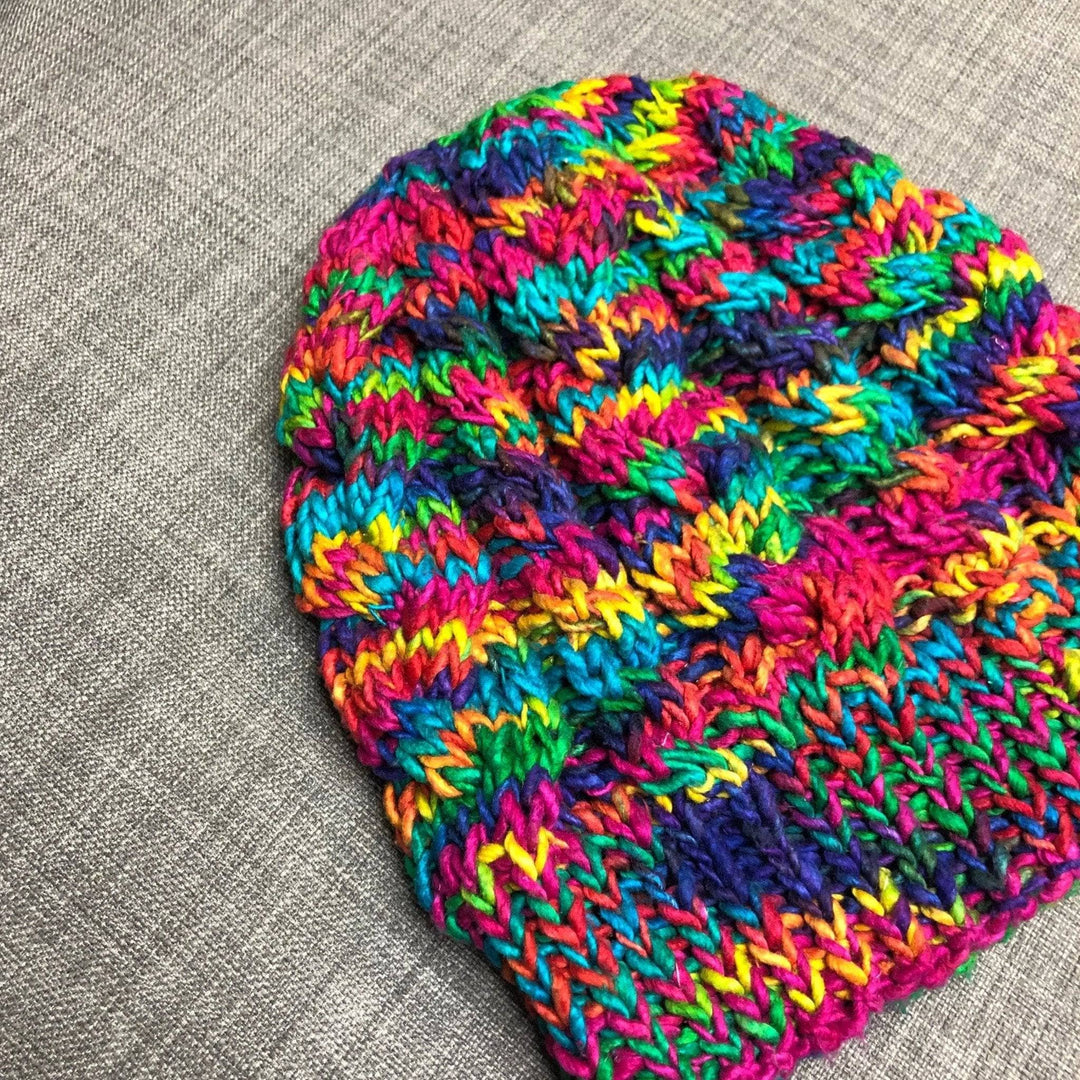 A colorful  Magnolia Beanie laying on a grey couch. 