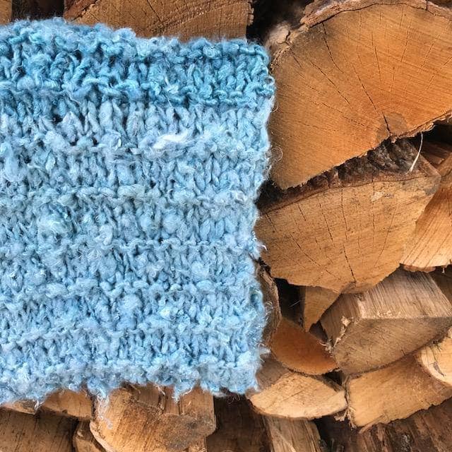 Close up of The Ocean Waves Cowl in Sea Mist (blue) on a wooden background