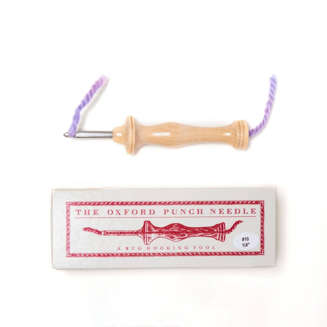 Oxford punch needle with purple yarn in channel along with the box the needle comes in in front of a white background.