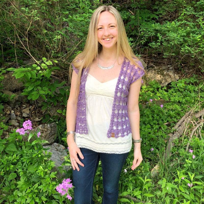 Woman wearing The Shenandoah Shrug in Purple standing in front of greenery