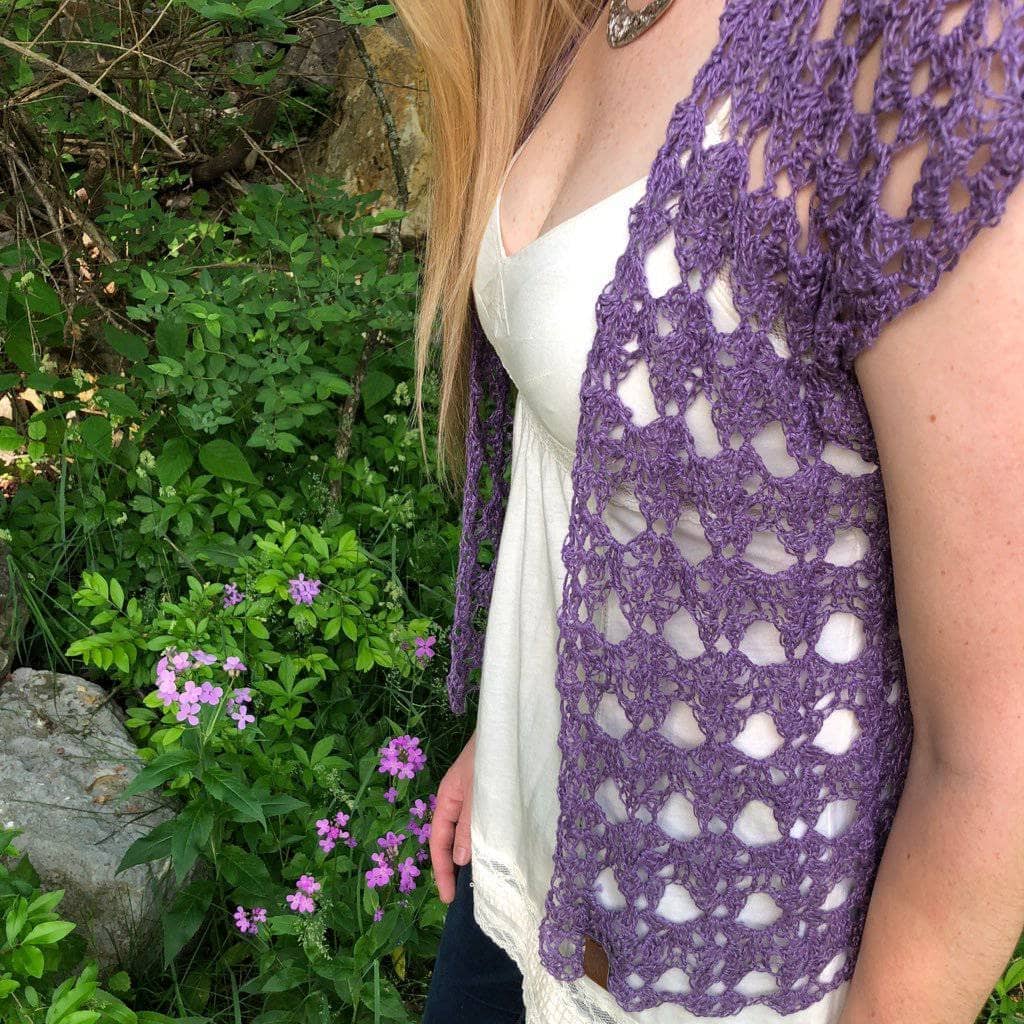 Woman wearing The Shenandoah Shrug in Purple standing in front of greenery